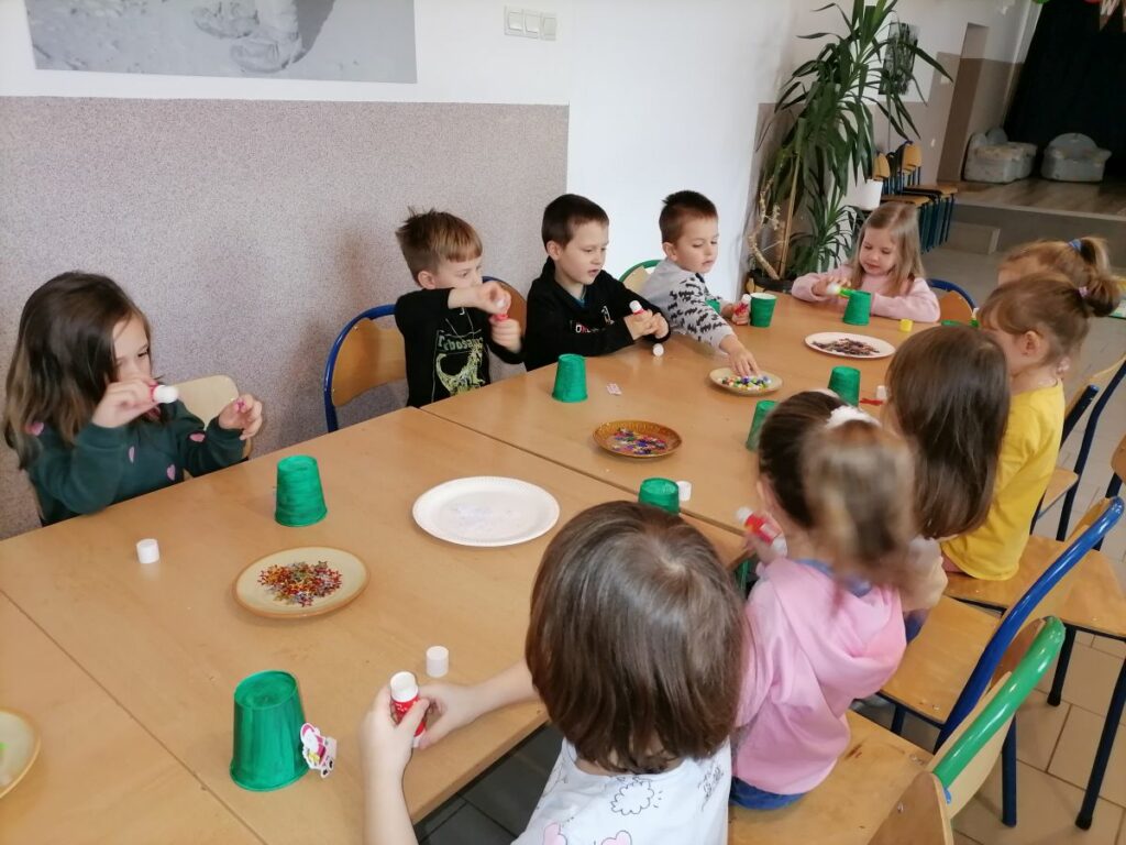 Przy długim stole siedza dzieci i przygotowują się do zajęć