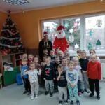 Na zdjęciu stoi bibliotekarz w czerwonej Mikołajkowej czapce oraz dzieci do wspólnego zdjęcia