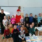 Grupa dzieci razem z panem bibliotekarzem oraz wykonaną z filcu postacią Świętego Mikołaja pozują do pamiątkowej wspólnej fotografii.