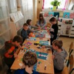 Dzieci pracują przy stole z wielkim zapałem nad swoimi kolorowymi bałwankami, wszędzie pełno jest rozłożonych przyborów plastycznych.