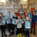 Pamiątkowe zdjęcie pana bibliotekarza z grupą uśmiechniętych dzieci biorących udział w sobotnich zajęciach. Każdy trzyma z dumą kartkę ze swoim pięknym bałwankiem.