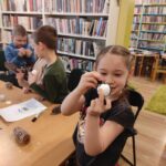 na zdjęciu widać dzieci siedzące przy stole, wykonujące pracę plastyczną na zdjęciu widać salę biblioteczna, regały z książkami, dzieci siedzą wokół stołu, na stole znajduje się globus
