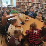 na zdjęciu widać dzieci siedzące przy stole, wykonujące pracę plastyczną na zdjęciu widać salę biblioteczna, regały z książkami, dzieci siedzą wokół stołu, na stole znajduje się globus