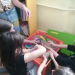 Na zdjęciu widać trzy dziewczynki, które siedzą przy małym stoliczku na którym jest piasek kinektyczny . Dziewczynki lepią różne figurki z piasku.