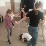 W sali świetlicy w Tyliczu dzieci bawią sie w kułeczku. Jedna dziewczynka kuca w środku.