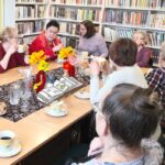 na zdjęciu widać sale biblioteczną, regały z książkami oraz stół przy którym siedzą panie seniorki.
