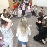 na fotografii widać salę przedszkolną oraz dzieci jedne siedzą inne stoją na beżowej wykładzinie