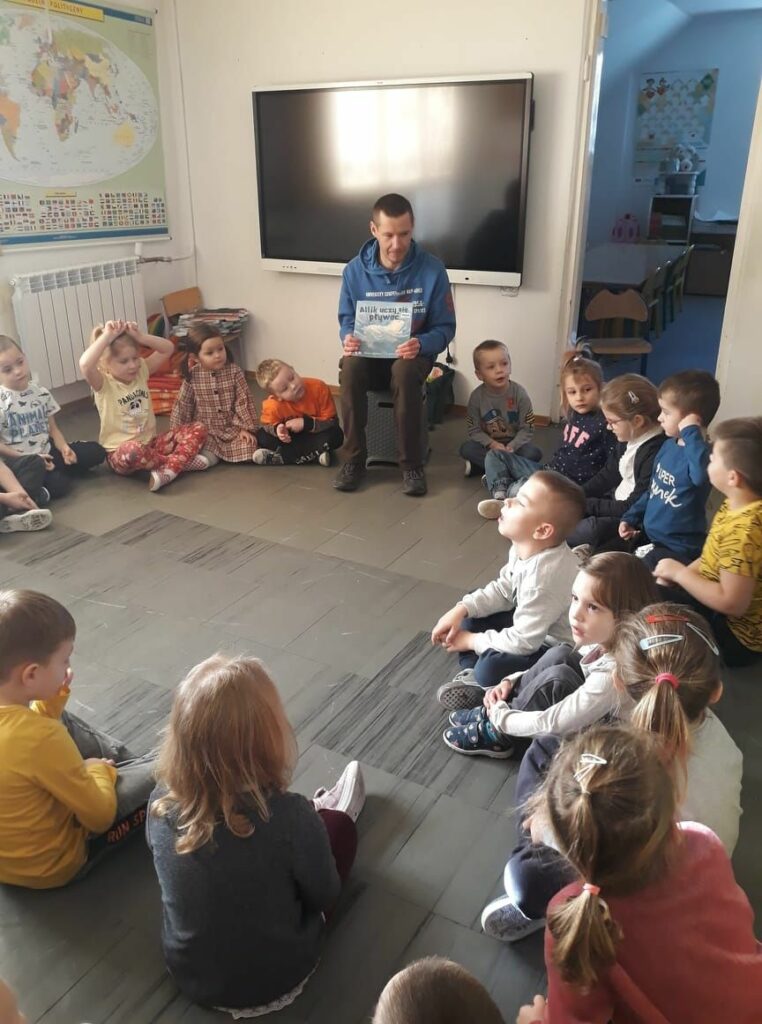 W przedszkolnej sali dzieci siedzą w kółeczku i słuchają z zainteresowaniem bajki o niedźwiadku polarnym Alfiku.