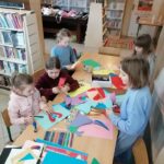 Uczestnicy spotkania pracują w skupieniu przy stole wycinając z kolorowego papieru serduszka, które przykleją do walentynkowych kartek.