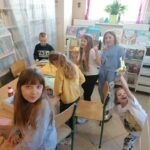 Grupa dzieci stoi przy bibliotecznym stole i wycina z papieru kolorowe kocie figurki.
