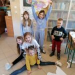 Uśmiechnięci uczestnicy spotkania pozują do pamiątkowej fotografii. Jedna z dziewczynek trzyma nad głową wykonaną przed momentem ogromną kocią poduchę.