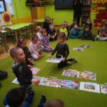 na zdjęciu widać kolorową sale przedszkolną, zieloną wykładzinę na której siedzą dzieci i układają kolorowe obrazki - ilustracje z bajek.