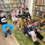 na zdjęciu widać salę biblioteczną, regały z książkami, na środku sali na dywanie siedzą dzieci