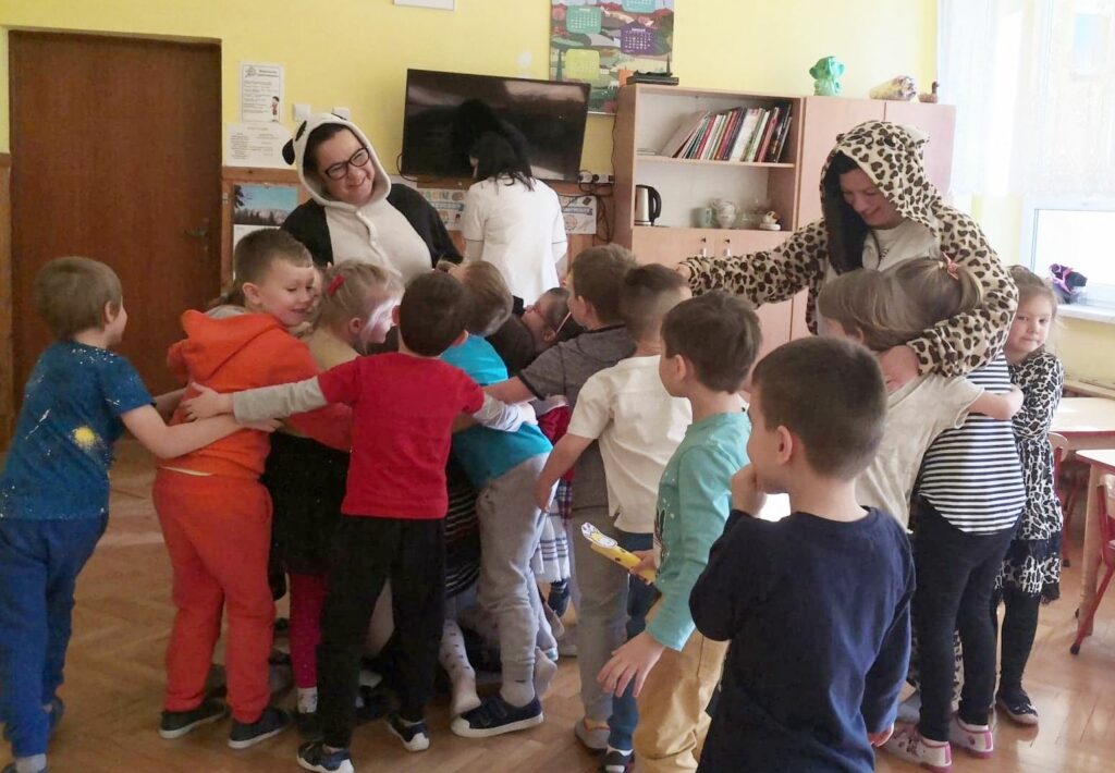 Na zdjęciu widać tulące się dzieci a wśród nich przebrane za zwierzaki bibliotekarki