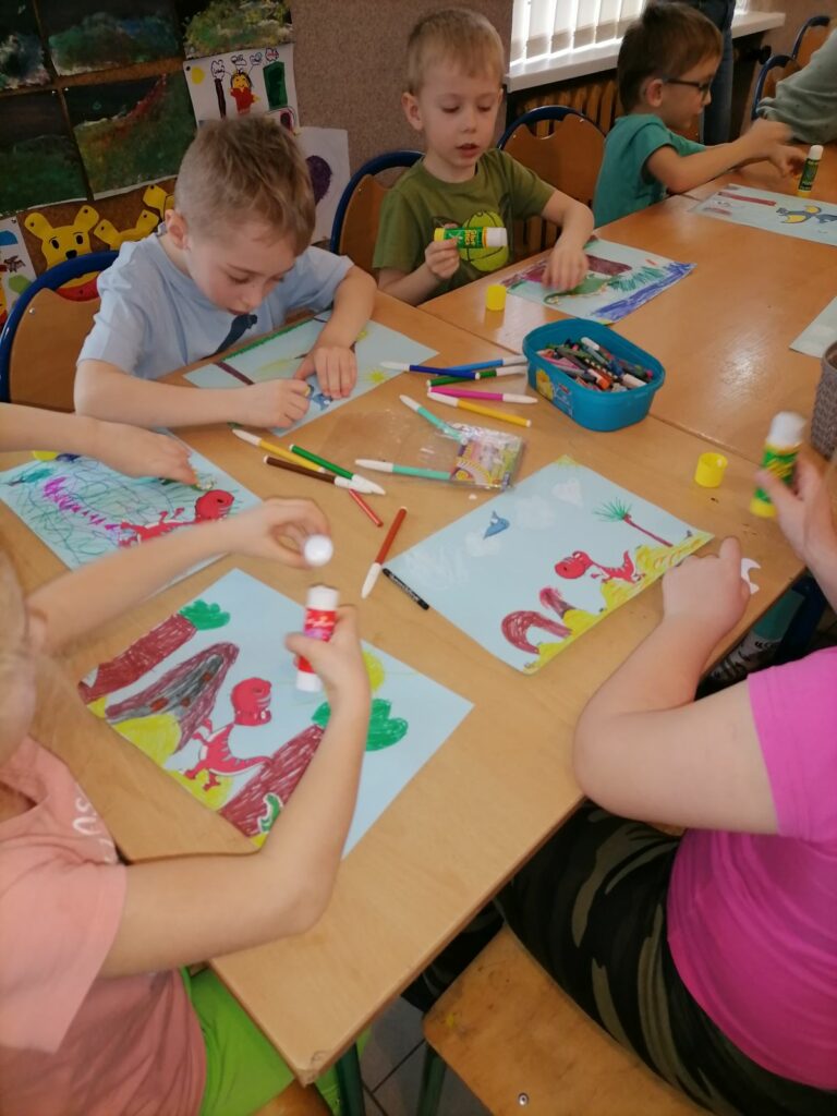 Na zdjęciu widocznych jest sześcioro przedszkolaków wykonujących pracę plastyczną pt. "Kraina dinozaurów" metodą kolażu.