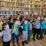 na zdjęciu widać salę biblioteczną, regały z książkami, na środku sali stoją przedszkolaki