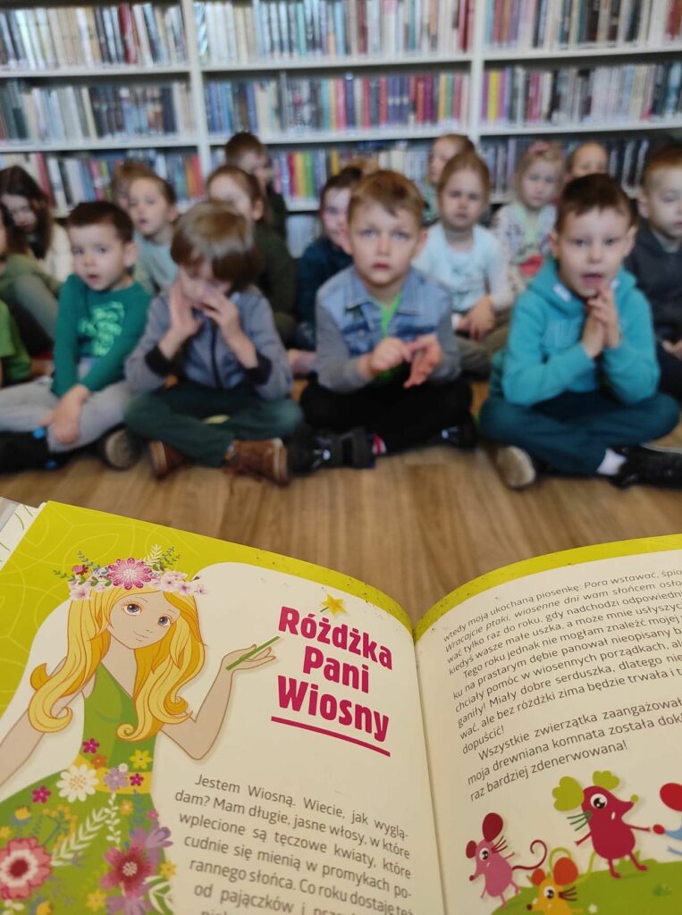 na zdjęciu widać fragment książki czytanej dzieciom, w tle widać dzieci
