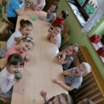Na zdjęciu widoczna jest grupa przedszkolaków siedzących przy stoliku i jedzących ozdobione przez siebie muffinki.