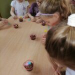 Na zdjęciu widoczna jest dziewczynka, która ozdabia swoją muffinkę kwiatkami z masy cukrowej.