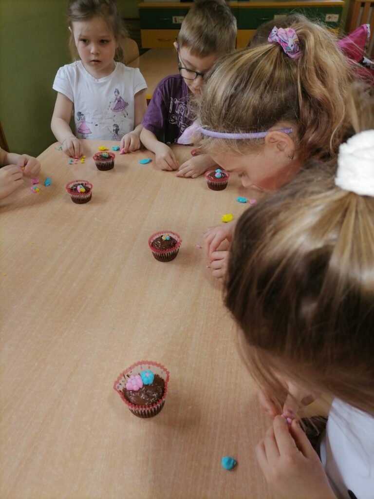 Na zdjęciu widoczna jest dziewczynka, która ozdabia swoją muffinkę kwiatkami z masy cukrowej.