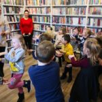 na zdjęciu widać dzieci, oraz dwie Panie. dzieci naśladują bibliotekarkę udając bociany.