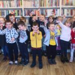 na zdjęciu widać dzieci stojące na tle regałów z książkami i trzymające wykonane przez siebie papierowe jaskólki.