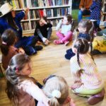 na zdjęciu widać dzieci siedzące na podłodze a wraz nimi siedzi bibliotekarka przebrana za rolnika.