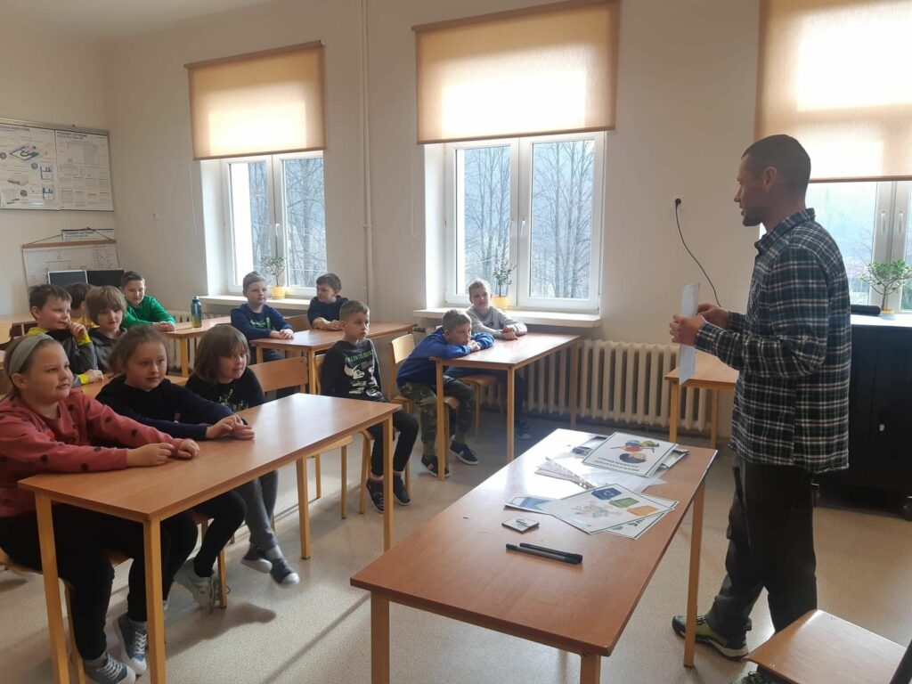 Grupa uczniów siedzi w ławkach i razem z panem bibliotekarzem omawia dekalog młodego ekologa.