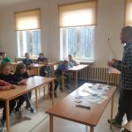 Grupa uczniów siedzi w ławkach i razem z panem bibliotekarzem omawia dekalog młodego ekologa.