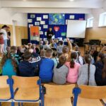 W szkolnej sali gimnastycznej siedzą przedszkolaki oraz uczniowie z najmłodszych klas. Dzieci ochoczo odpowiadają na zadawane im przez pana bibliotekarza ekologiczne zagadki i rebusy.