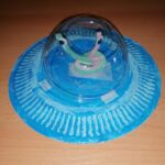 Na zdjęciu widać z bliska niebieski statek Ufo z siedzącym w środku pilotem ufoludkiem