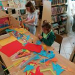 Dzieci pracują przy zapełnionym materiałami plastycznymi stole wycinając i klejąc swoje piękne papierowe motyle.