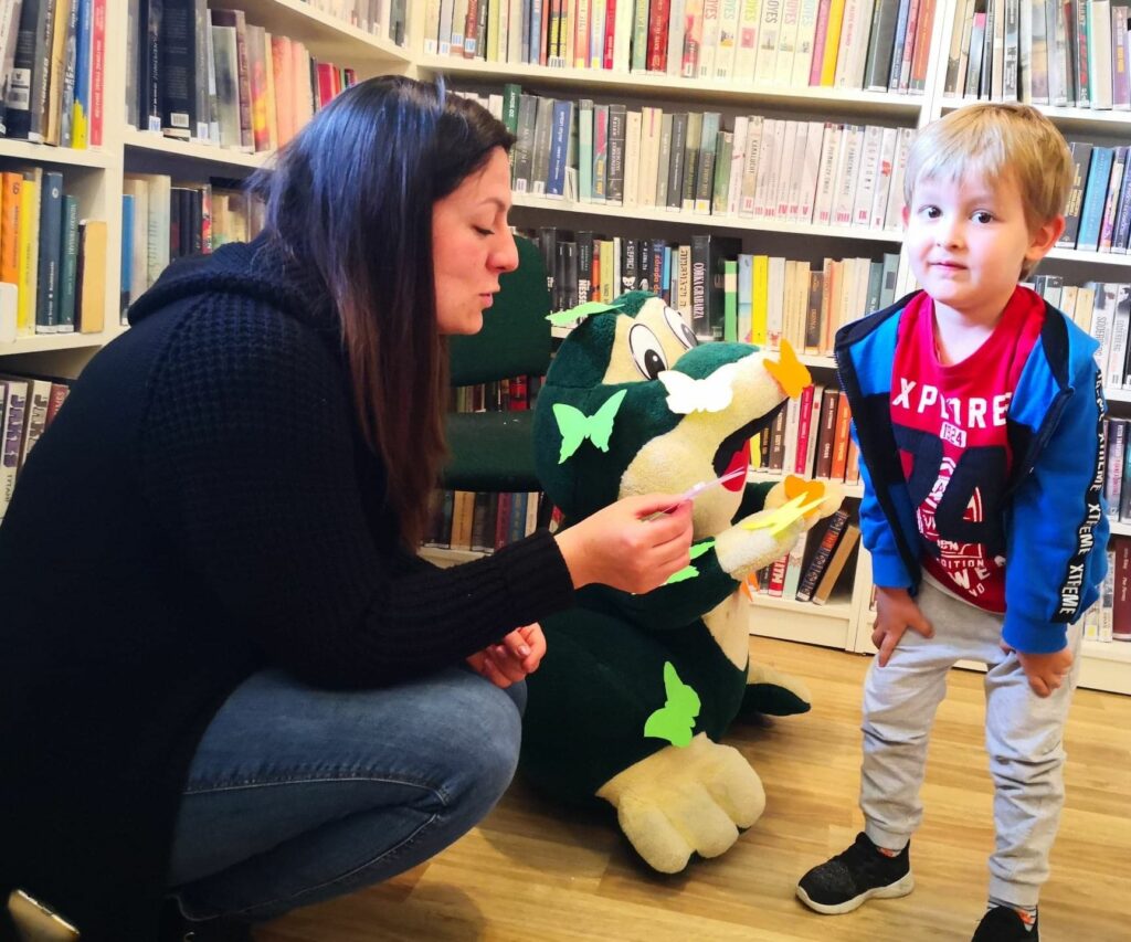 na zdjęciu widać pluszową żąbe na niej kolorowe motylki oraz chłopca i bibliotekarkę