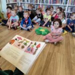 na zdjęciu widać dzieci siedzące na podłodze i słuchające czytanej im bajki