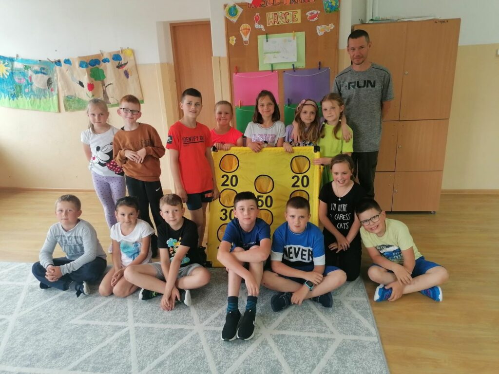 Pamiątkowe zdjęcie jednej z klas biorącej udział w spotkaniu. Uczniowie razem z panem bibliotekarzem stoją obok siebie, a pomiędzy nimi znajduje się żółta tarcza.