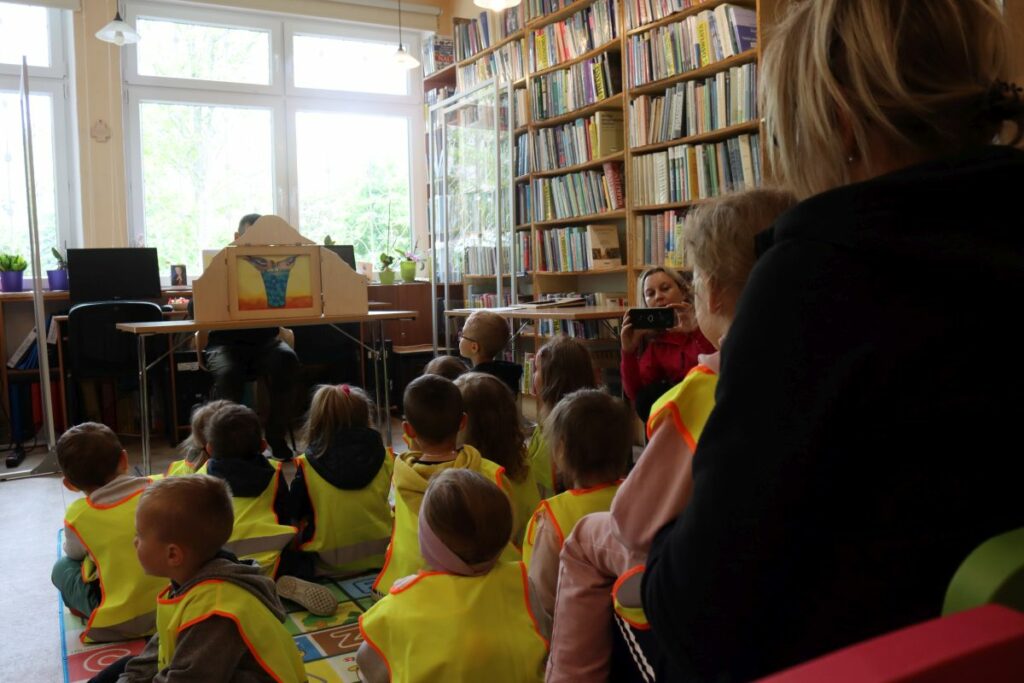 W sali bibliotecznej przy stole siedzi bibliotekarz