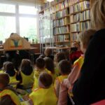 W sali bibliotecznej przy stole siedzi bibliotekarz