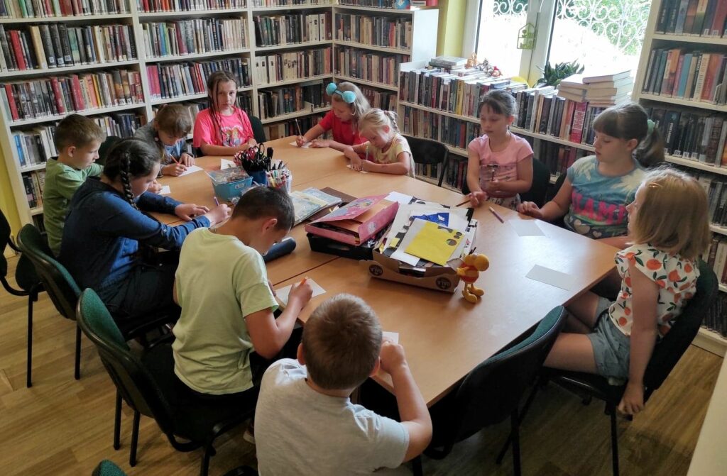 na zdjęciu widać dzieci pracujące przy stole w sali bibliotecznej