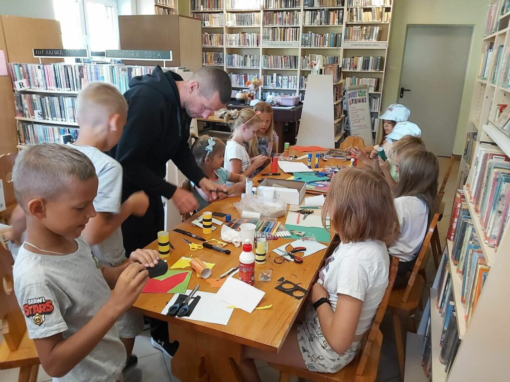 Dzieci pracują przy stole tworząc z rolek papieru toaletowego różne owady i zwierzątka. Do pomocy mają m.in. papier kolorowy, klej, bibułę i kredki.