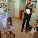 Jedna z dziewczynek pisze na wiszącym na stelażu plakacie, czego nie można robić w lesie. Obok niej stoi pan Leśnik i opowiada m.in. o zakazie śmiecenia w lasach.