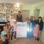 Wszystkie dzieci ustawiły się wokół pana Leśnika. Pomiędzy nimi stoi narysowany wspólnie wielki plakat pt. „Dobre leśne wychowanie”. Uczestnicy trzymają w rękach podstawowy sprzęt używany w pracy Leśnika czyli np. kask ochronny, kulpę do pomiarów i numerator - przyrząd do oznaczania ściętych drzew.