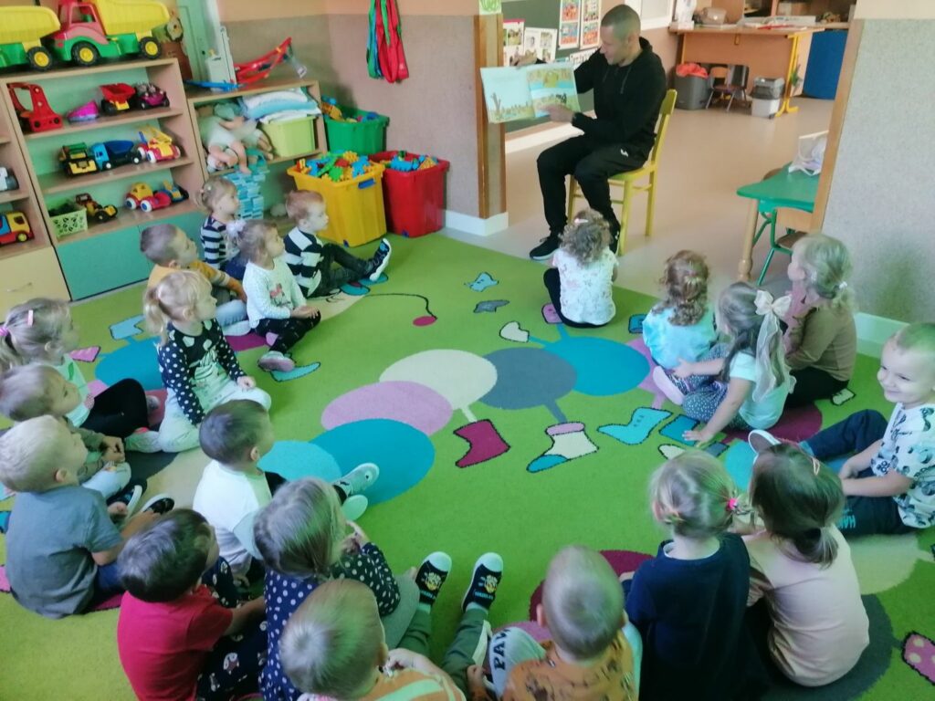 W przedszkolnej sali dzieci siedzą w kółeczku i słuchają z zainteresowaniem bajki o „Złotej Rybce” z Afryki.