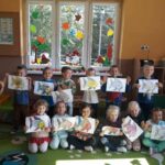 Grupa przedszkolaków ustawiła się do zdjęcia. Każde dziecko trzyma w rękach pięknie pokolorowany rysunek „Złotej Rybki”.