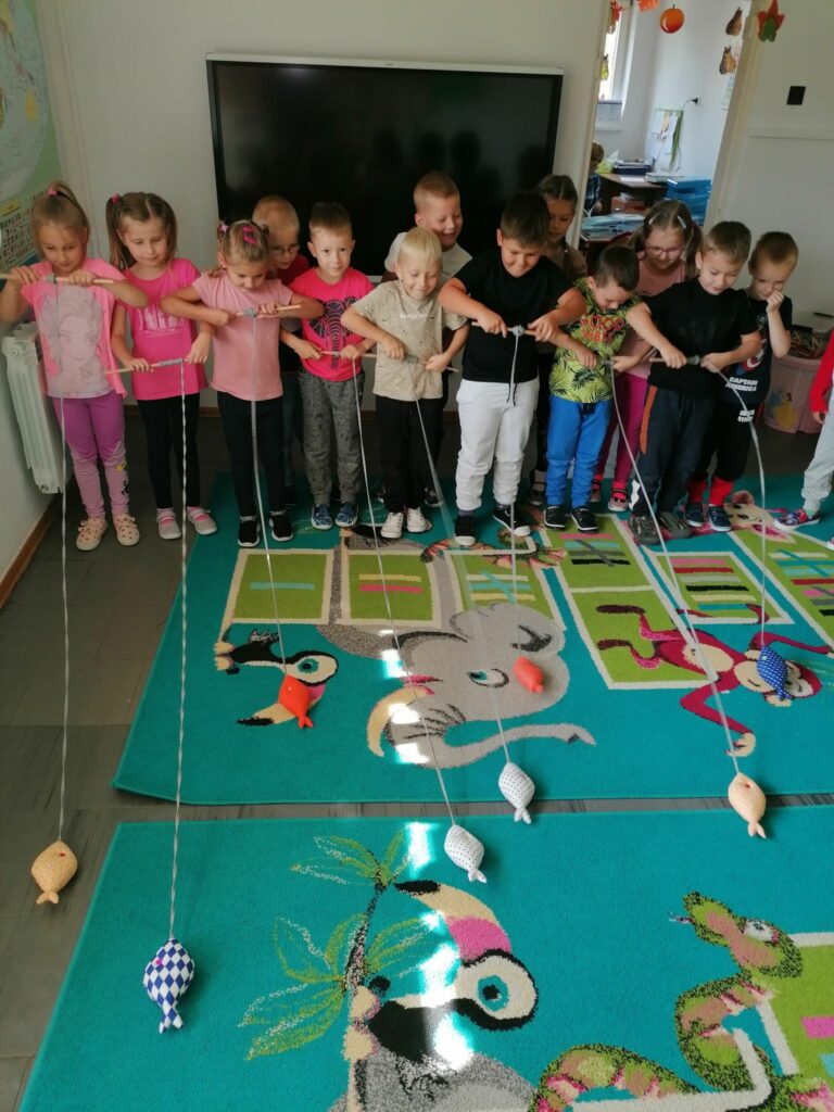 W grupie „starszaków” właśnie trwają zawody wędkarskie. Uczestnicy na wyścigi nawijają na patyczki linki, do których na końcu przyczepione są małe, kolorowe rybki.