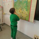 Na ścianie obok tablicy wisi wielka kolorowa mapa naszego kraju. Tuż przy niej stoi ubrany w zielony dres chłopiec i skoncentrowany szuka najgłębszego polskiego jeziora Hańcza.