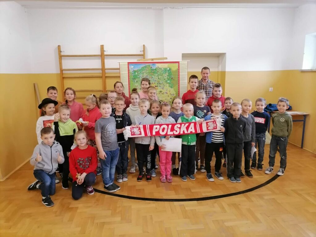 Wszystkie dzieci biorące udział w patriotycznych warsztatach ustawiły się razem z panem bibliotekarzem do pamiątkowego zdjęcia na tle wiszącej za ich plecami mapy.
