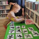 na zdjęciu widać dziewczynkę stojąca przed zielonym stolikiem na którym poukładano czarno-białe obrazki.