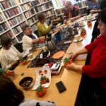Na zdjęciu widać seniorki siedzące wokół stołu w sali bibliotecznej