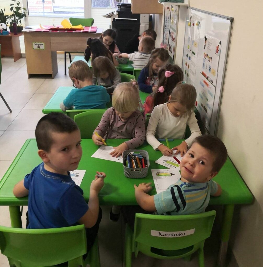 na zdjęciu widać sale przedszkolną oraz dzieci siedzące przy zielonych stolikach