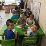 na zdjęciu widać sale przedszkolną oraz dzieci siedzące przy zielonych stolikach